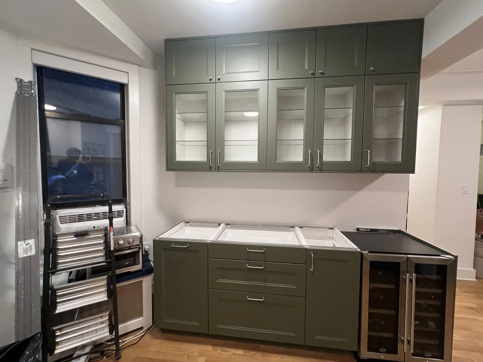 Sage green IKEA kitchen with glass-front cabinets and wine cooler
